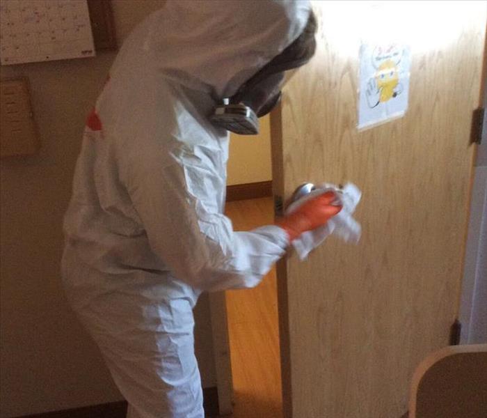 Man in PPE cleaning a door in a commercial facility